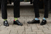 two men showing off their colorful socks while wearing black pants and black shoes