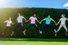 five people jumping up while holding hands in front of a hedge showing off their seasonal socks